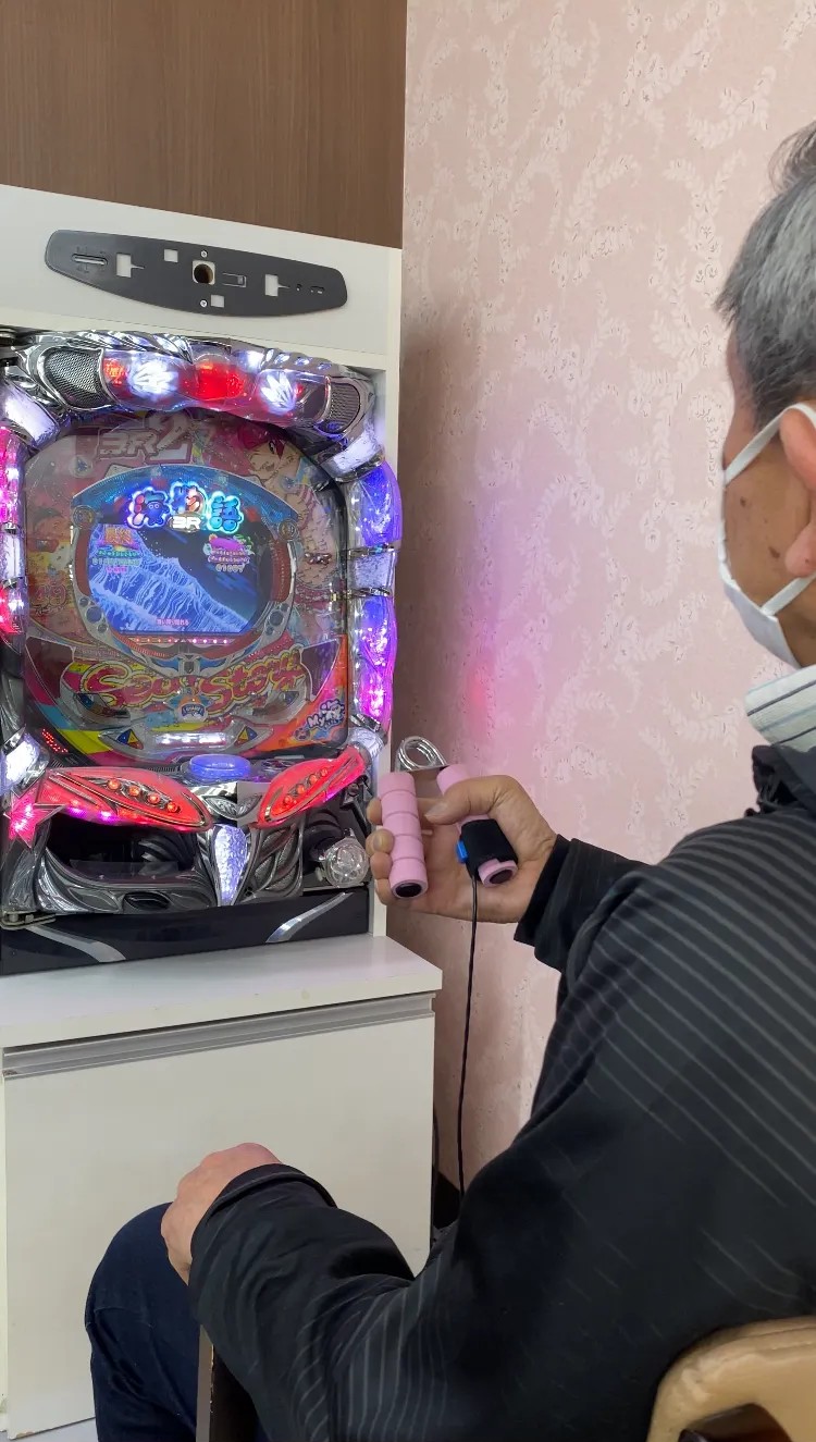 福祉施設でハンドグリップを使いながらパチンコを操作する機能訓練の様子