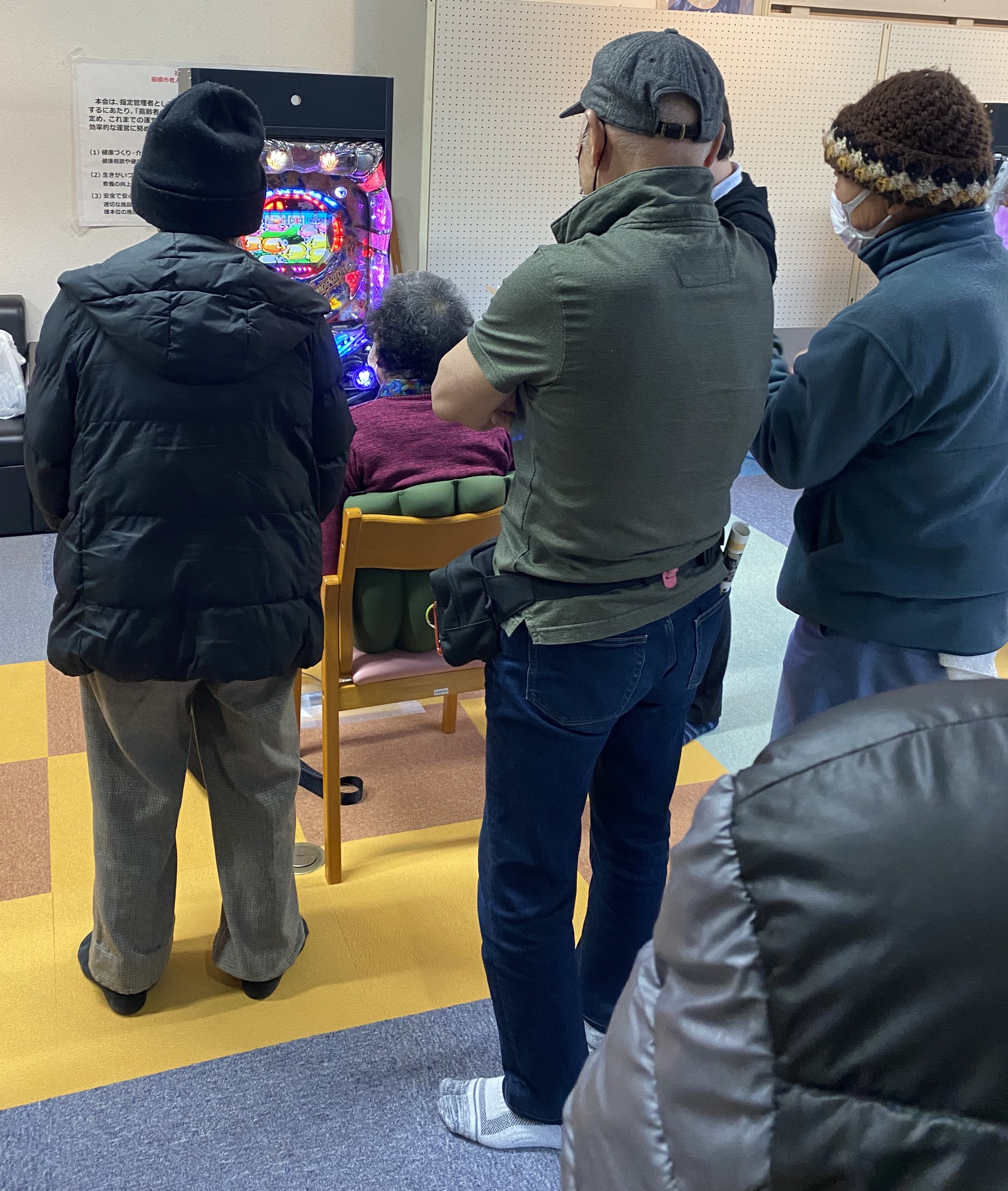 介護施設で複数人が介護予防用パチンコを囲み応援している様子（集団レク）