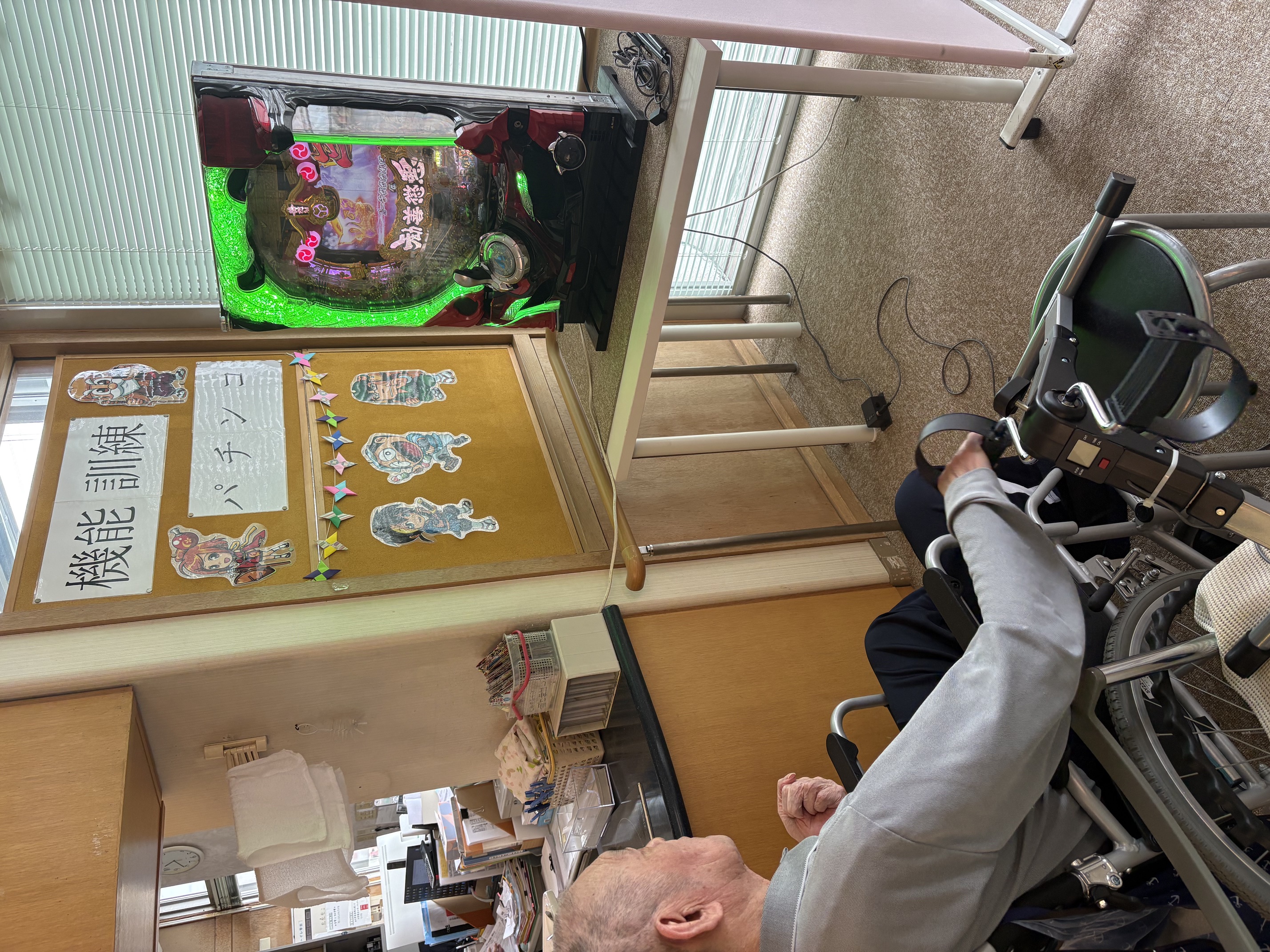 みどりデイサービスセンターで車いすの利用者様が機能訓練器具を使いながらパチンコに取り組む様子