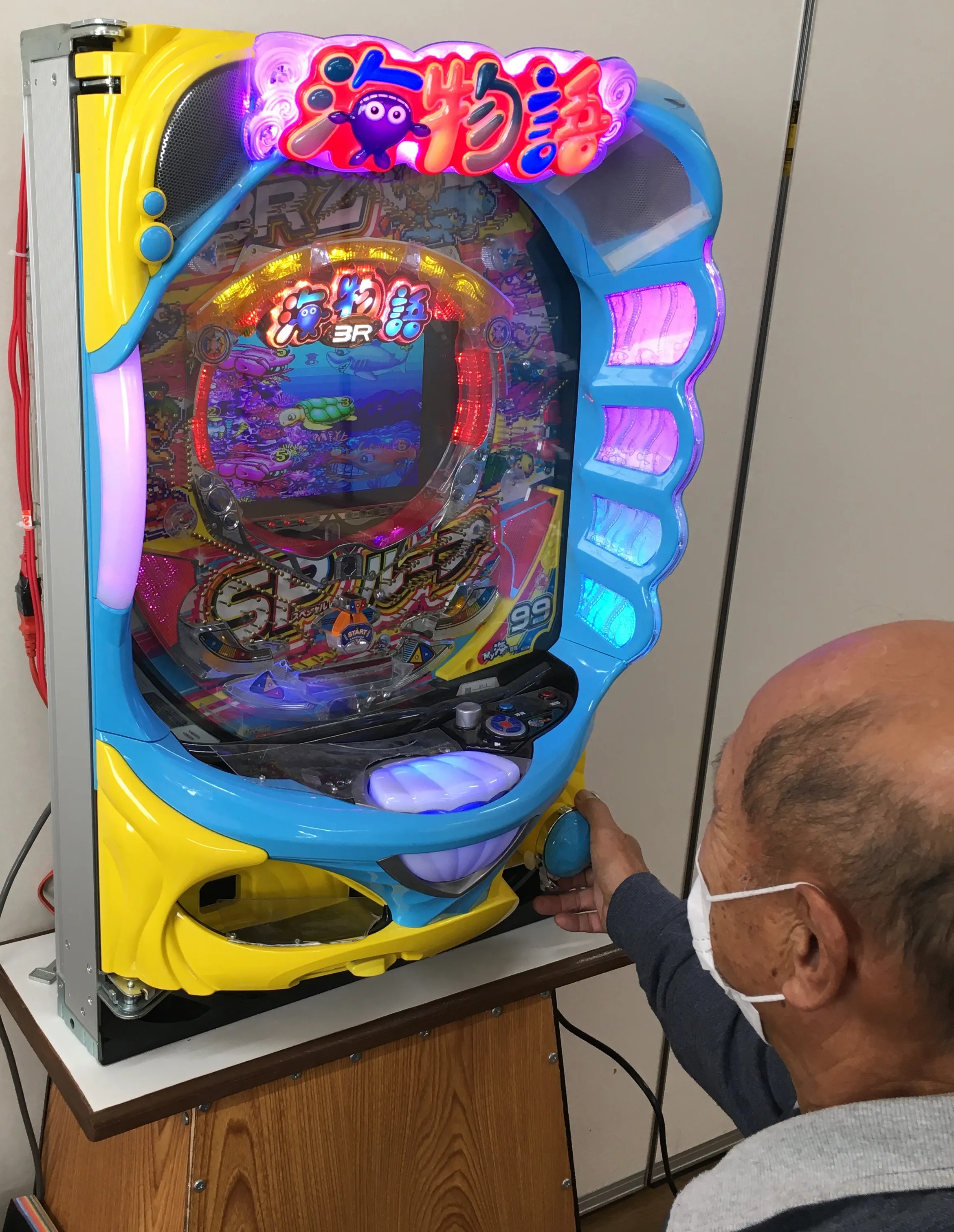 介護施設で複数人がパチンコ型の機能訓練機器を見守りながら楽しんでいる様子